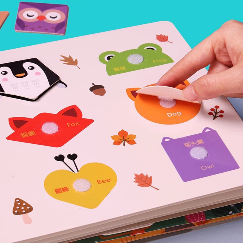 Children's educational book with removable animal shapes. A hand lifts the "Dog" piece, revealing a Velcro spot. Other visible shapes include Fox, Bee, Frog, and Owl, with playful graphics.
