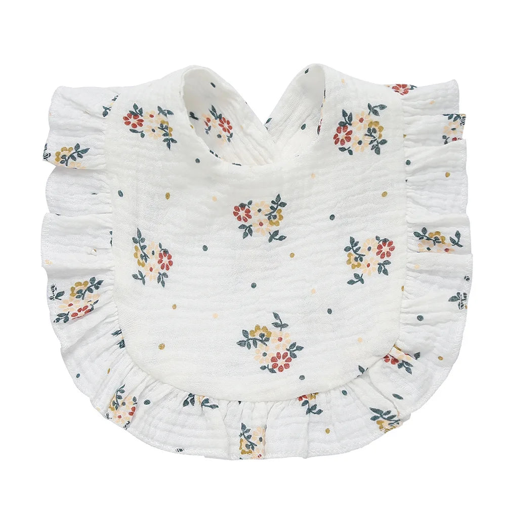 A white bib with a floral print of red, yellow, and blue flowers, featuring ruffled edges. The fabric has a textured appearance, adding a delicate touch to the design.
