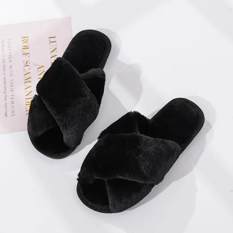 Black fur slides with crisscross straps on a light surface. A piece of paper is partially visible in the background, adding a soft contrast to the plush slippers.
