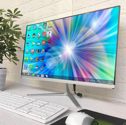 A sleek desktop monitor on a white desk displays vibrant, colorful rays on the screen. A white keyboard and mouse sit below, with a potted plant positioned to the left.