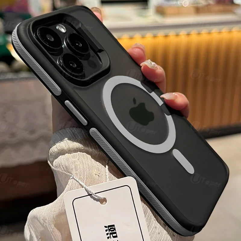 A hand holds a smartphone with a black case that features a large camera cutout and a circular white MagSafe ring around an Apple logo. A tag is attached at the bottom.
