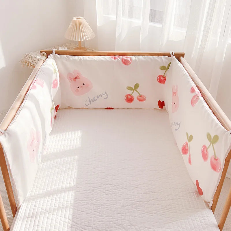 A cozy crib with white quilted bedding, surrounded by soft bumpers featuring pink bunnies and cherries. A small lamp sits on a lace-covered table, with sunlight filtering through sheer curtains.