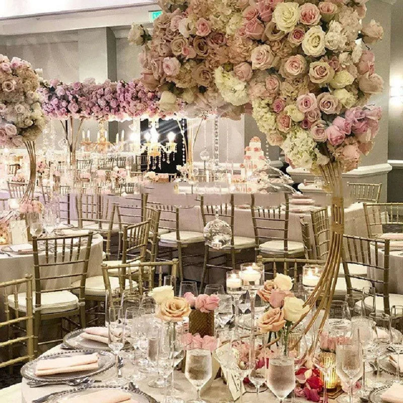 Elegant wedding reception with tables adorned in pink and white flowers, gold chairs, and sparkling candlelight. Floral arches decorate the room, creating a romantic ambiance.
