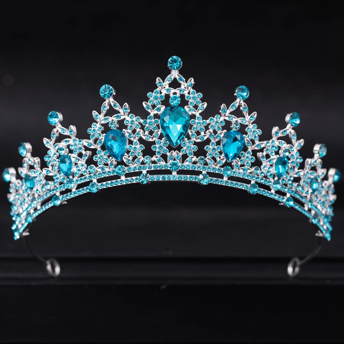 A sparkling tiara adorned with intricate silver detailing and dazzling blue gemstones, set against a dark background.
