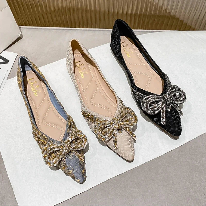 Three elegant flat shoes with large glittering bows in blue, beige, and black, displayed on a white surface.
