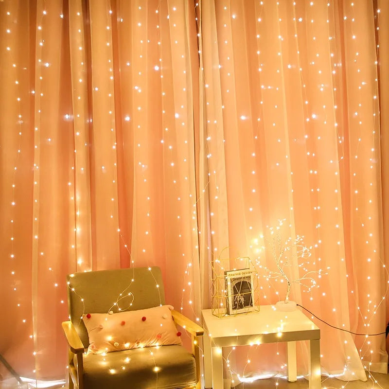 Cozy room with pink curtains adorned with warm fairy lights. An armchair with a pink pillow is beside a white table holding a decorative light and a book.
