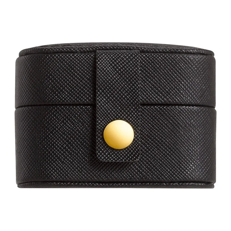 Black textured cylindrical jewelry case with a gold button closure on a strap.
