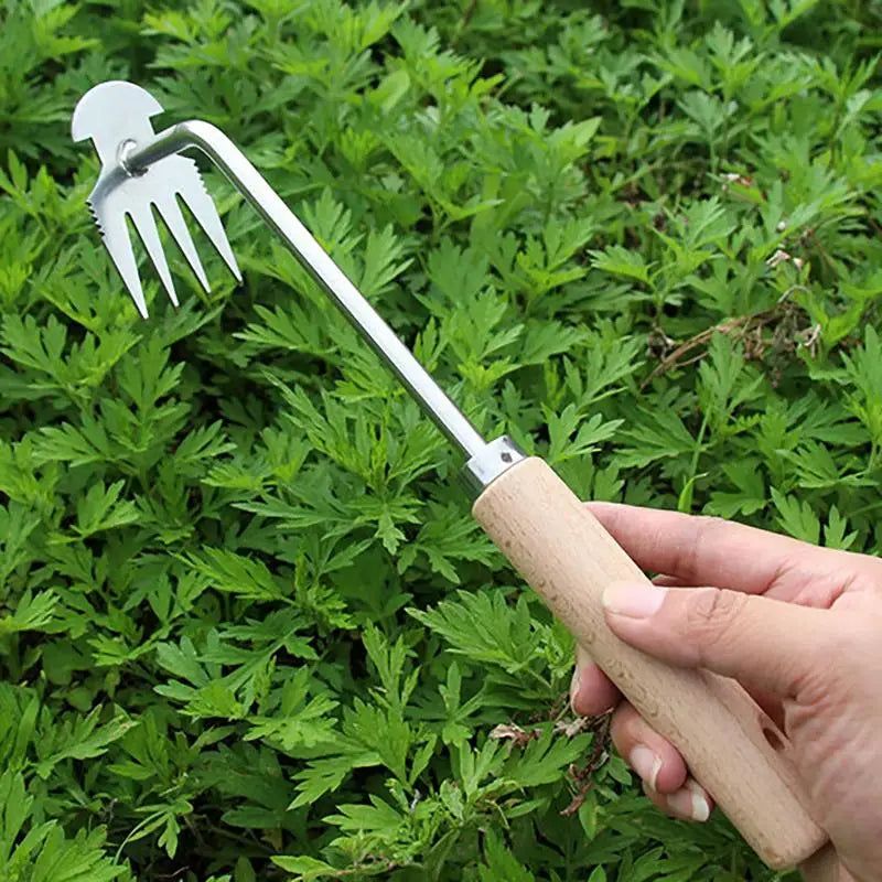 A hand holding a garden weeder with a wooden handle and metal prongs over lush green foliage, ready for gardening tasks.