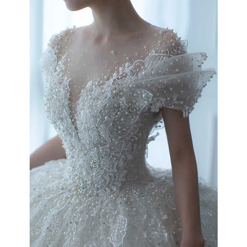 Close-up of a woman in an elegant wedding dress adorned with pearls and intricate lace, featuring an off-the-shoulder design and a layered, voluminous skirt.