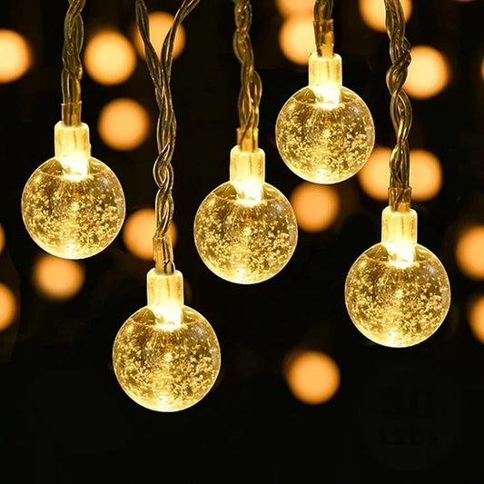 Five glowing, round, golden string lights hang in front of a dark background, creating a warm, sparkling ambiance with reflections inside each bulb, resembling festive decor.
