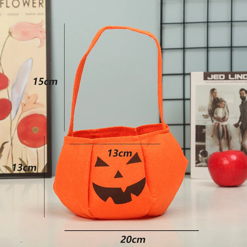 Orange felt Halloween basket shaped like a pumpkin with a black jack-o'-lantern face, measuring 20cm wide, 13cm tall, and a 15cm handle. Background includes artwork and a red apple.