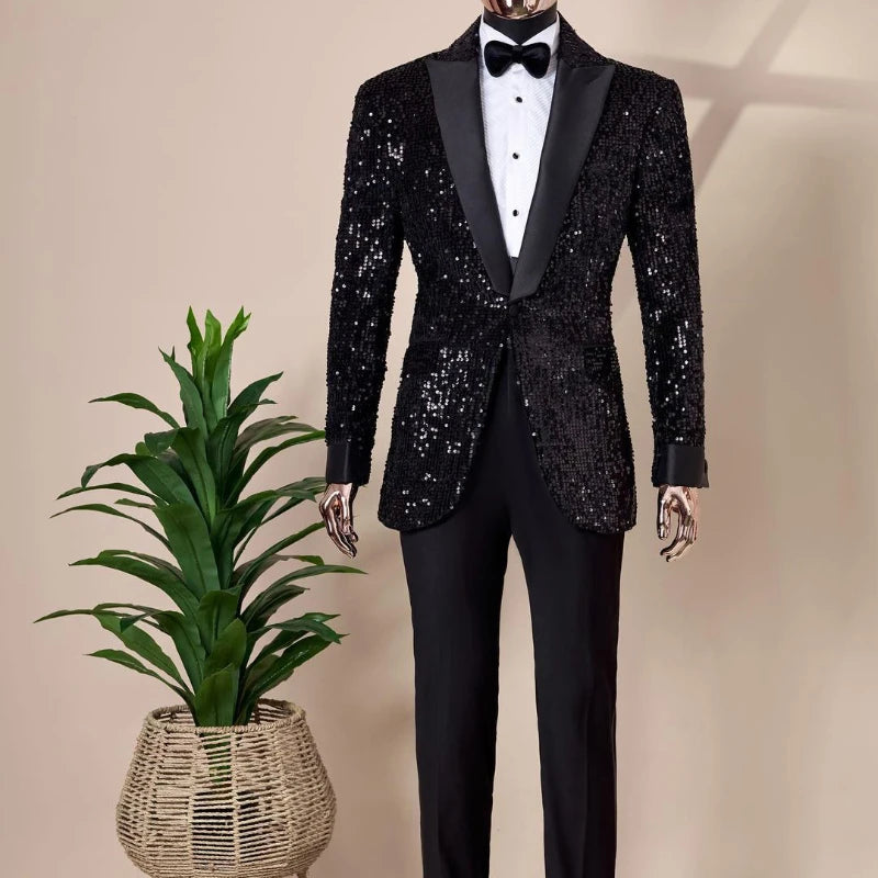 A mannequin displays a black sequined tuxedo with satin lapels and a white shirt, accented by a black bow tie. Beside it is a green plant in a woven basket.