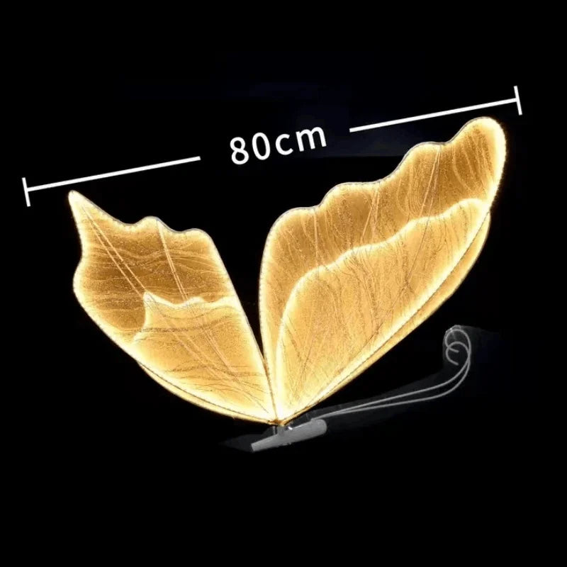 Glowing gold ginkgo leaf wall light, measuring 80cm, with illuminated veins. Mounted on a dark background, its curved design resembles butterfly wings.