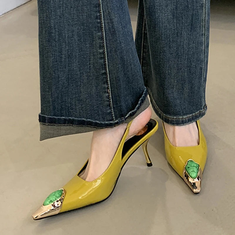 Yellow slingback heels with gold-pointed toes and green embellishments, paired with blue jeans on a beige floor.