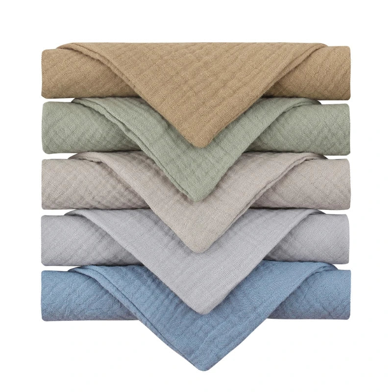 A stack of six folded towels in varied colors: tan, green, beige, light gray, gray, and blue. Each towel is evenly layered with the edges neatly aligned.
