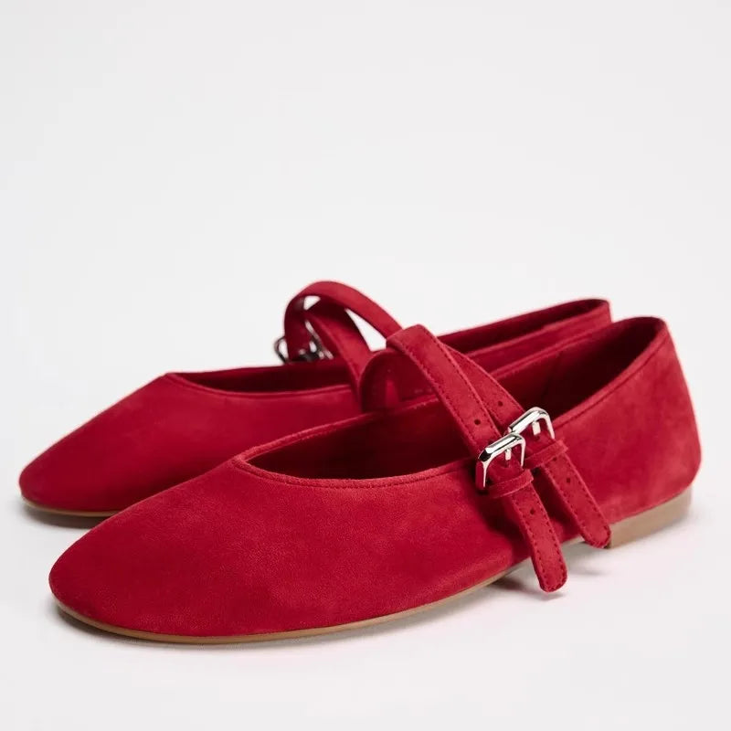 Red suede ballet flats with adjustable ankle straps and silver buckles, featuring a rounded toe and flat soles, positioned against a plain white background.
