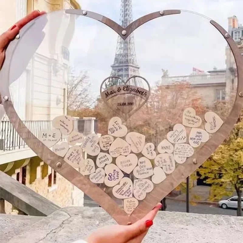 Heart-shaped guestbook with wooden hearts inside, inscribed with messages. Eiffel Tower in the background. Hands holding it, capturing a romantic Parisian setting.