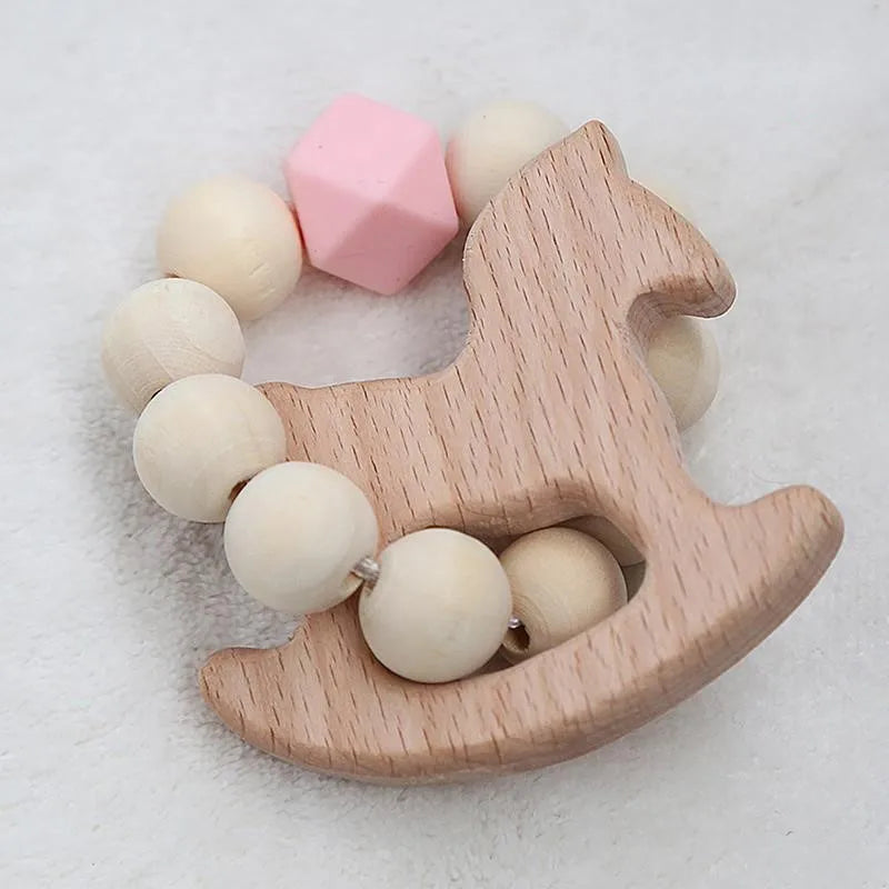 Wooden horse-shaped teether ring with light wood beads and a pink geometric bead, resting on a soft white surface.