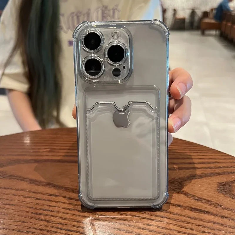 A person holds a smartphone with a clear protective case, featuring an embedded Apple logo. The phone has a triple-camera setup and is displayed above a wooden table.