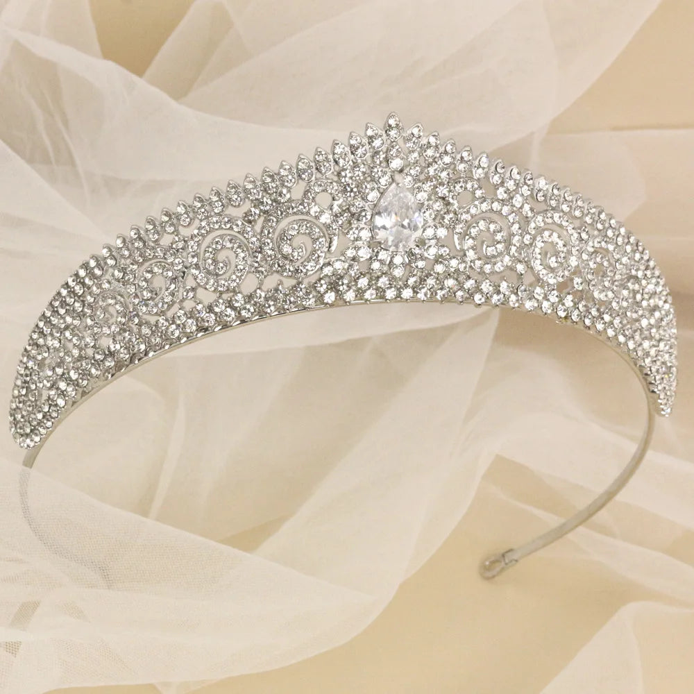 Sparkling tiara adorned with intricate patterns of clear crystals, set against a soft, sheer fabric backdrop. The design features a central teardrop-shaped gem.