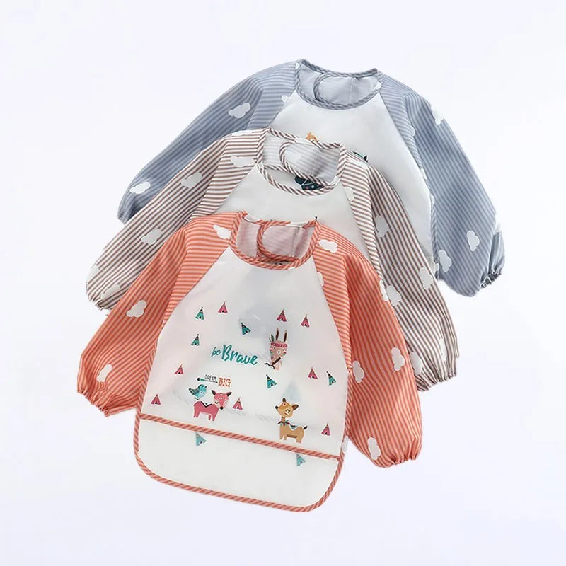 Three long-sleeved bibs with cloud designs. One is gray, another beige, and the front one is orange with playful animal prints and "be brave" text.