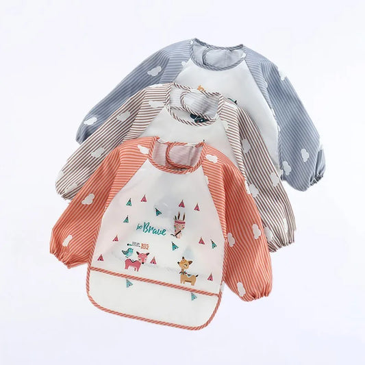 Three long-sleeved bibs with cloud designs. One is gray, another beige, and the front one is orange with playful animal prints and "be brave" text.