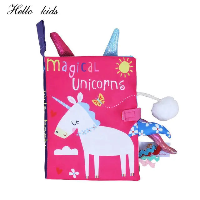 Pink children's fabric book titled "Magical Unicorns" featuring a white unicorn with a sun and butterfly. Includes colorful tags and textured attachments for sensory play.