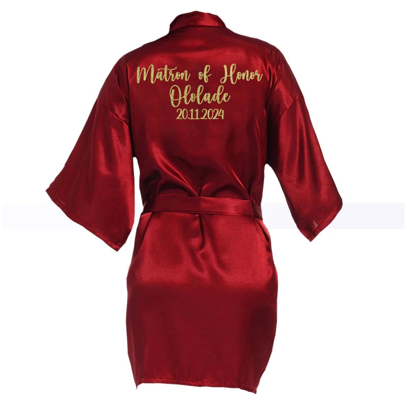 Red satin robe with "Matron of Honor Ololade 20.11.2024" in gold script on the back. The robe has loose sleeves and a tied belt, displayed against a white background.