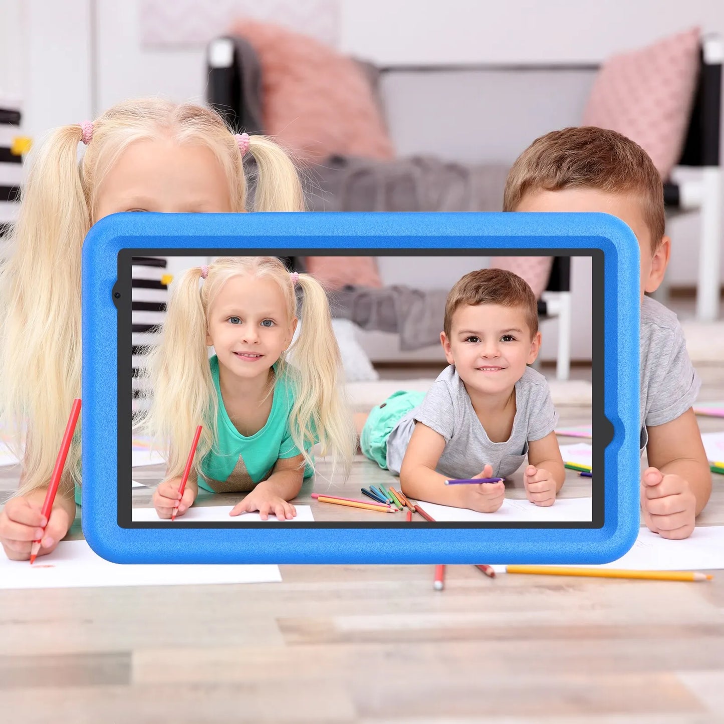 Two young children lie on the floor, drawing with colored pencils. A tablet frame captures both inside its screen, emphasizing creativity and technology in a cozy, playful setting.