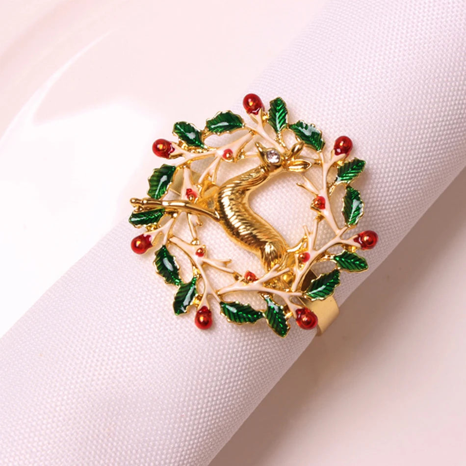 A decorative napkin ring featuring a gold reindeer and a wreath adorned with green leaves and red berries, wrapped around a white napkin on a plate.