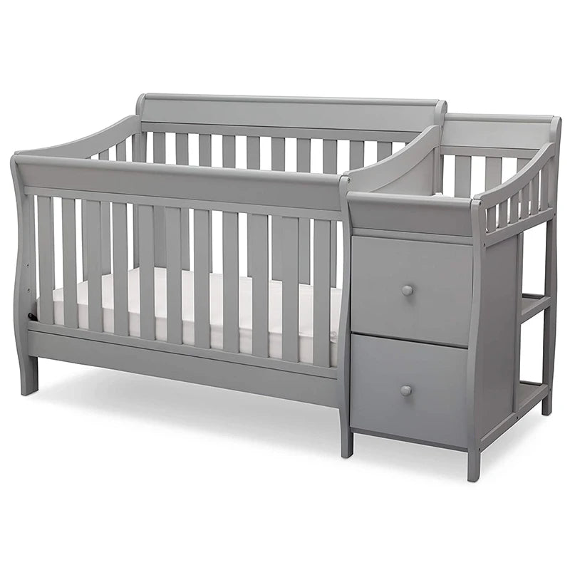 Gray wooden baby crib with a slatted design, attached changing station including two drawers, and a small shelf on the side.