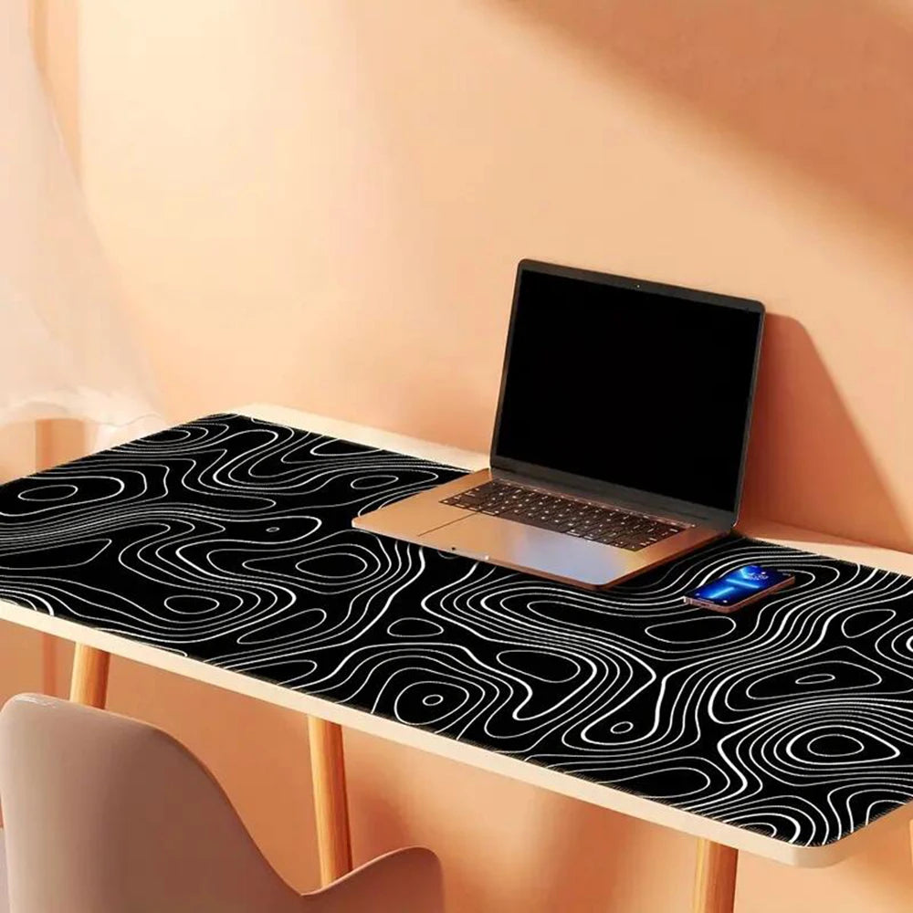 Laptop on a desk with a black and white abstract wavy pattern, a smartphone beside it. The desk and chair are against a warm, peach-colored wall with soft lighting.