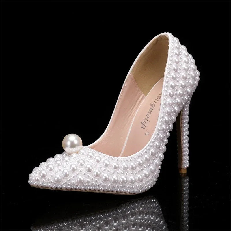 Elegant high-heeled shoe adorned with small white pearls and a large pearl on the toe, set against a black background, showcasing a contrast between glossy embellishments and sleek design.