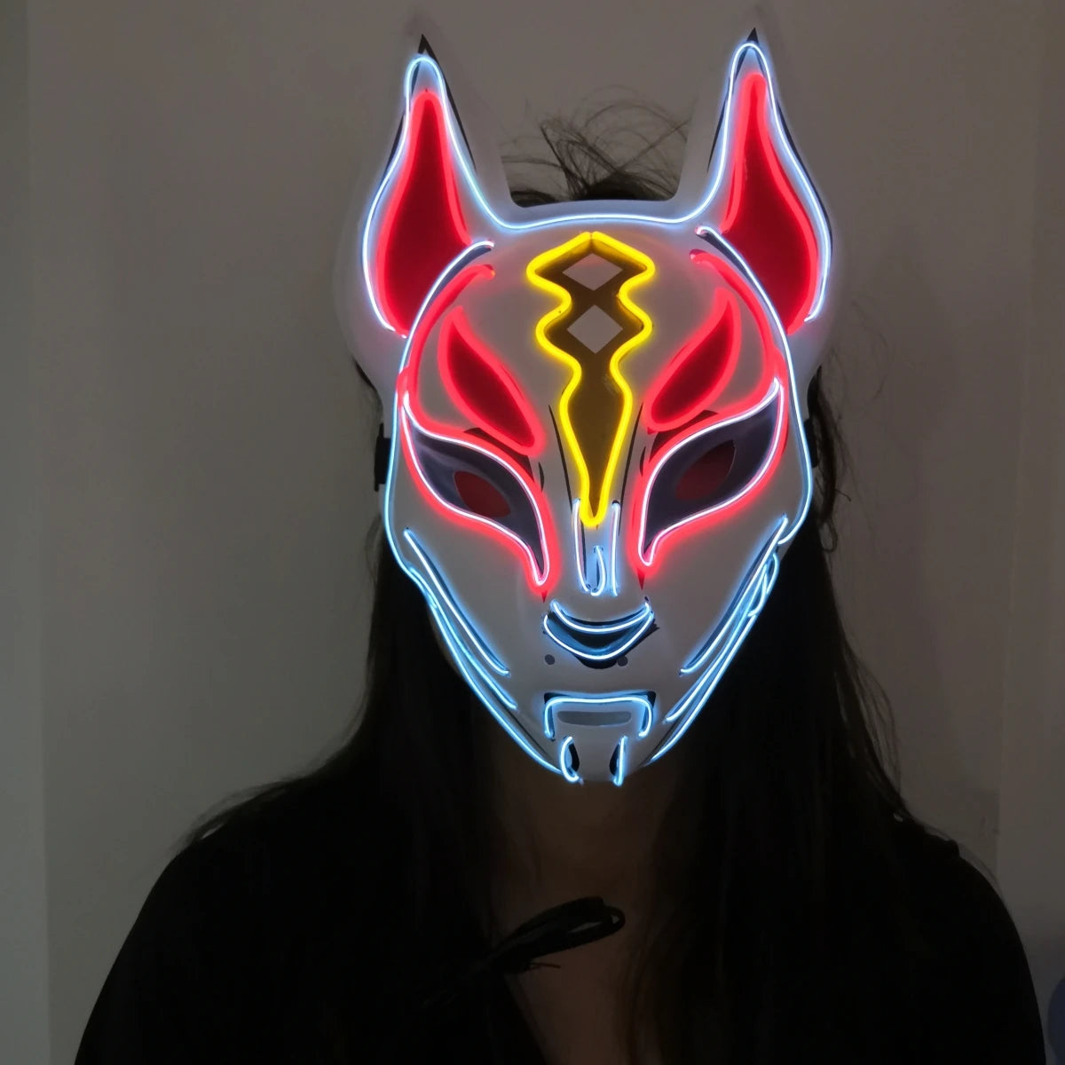 A person wearing a glowing fox mask with neon blue, red, and yellow lights highlighting the ears and eyes, set against a dark background.