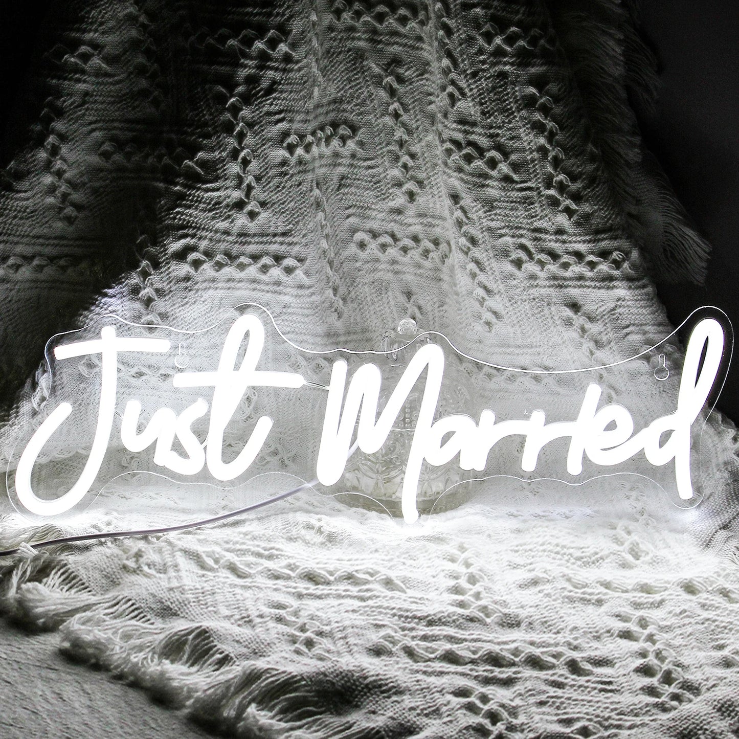 "Just Married" neon sign glows brightly against an intricate, white textured fabric background, creating a festive and romantic ambiance.