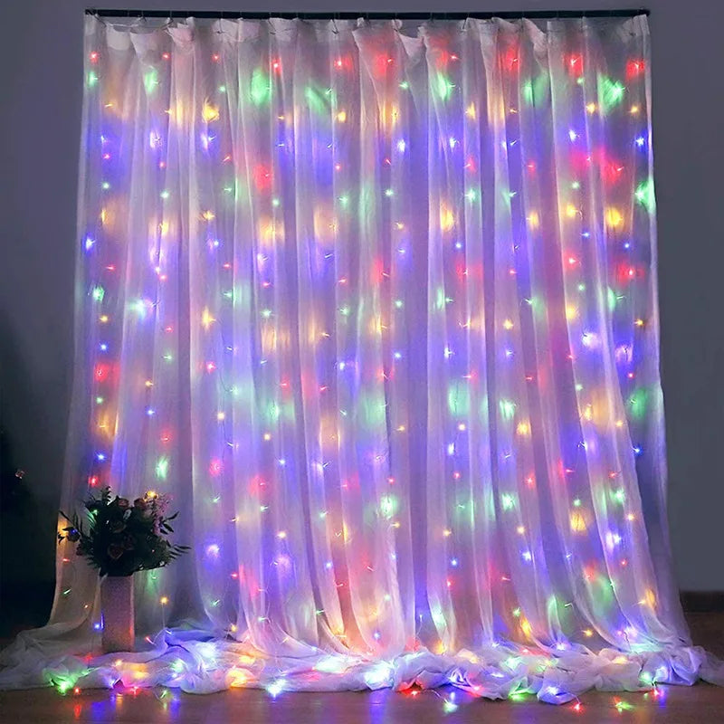 Colorful string lights draped over sheer white curtains, creating a soft, glowing effect. A small bouquet of flowers sits at the base to the left.