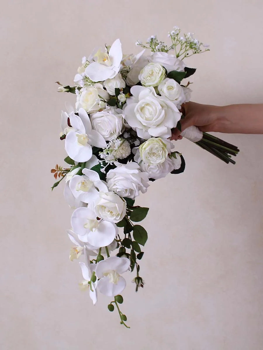 A cascading bouquet of white roses, orchids, and delicate greenery is held against a soft beige background, creating an elegant and serene floral arrangement.