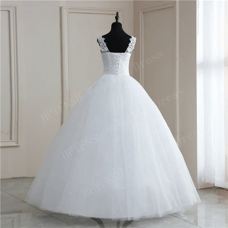 A white ball gown dress with floral lace straps displayed on a black mannequin in a bright room with soft natural lighting from a window on the right.
