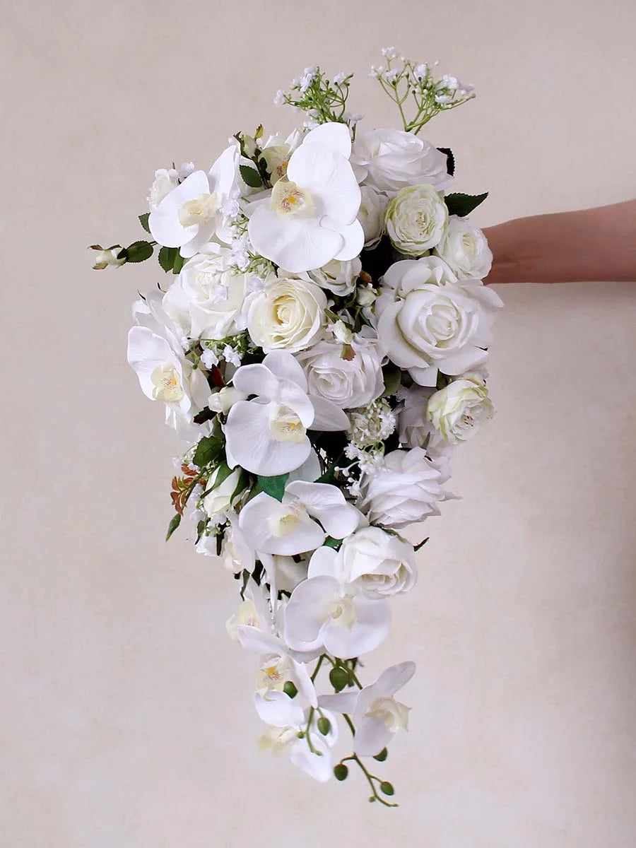 A cascading bouquet of white orchids, roses, and baby's breath, held by a hand against a plain background. The flowers are lush and elegantly arranged.