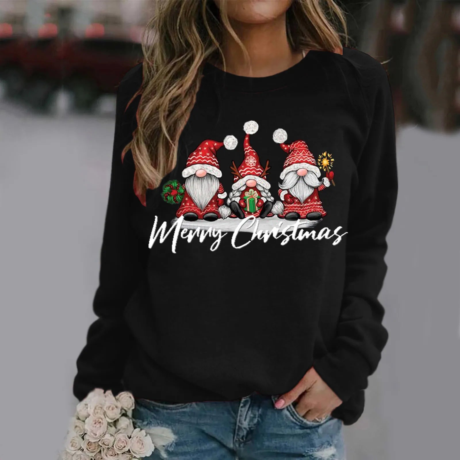 Woman wearing a black sweater with Christmas gnomes and "Merry Christmas" on the front, holding white roses. The gnomes have red hats and festive decorations.
