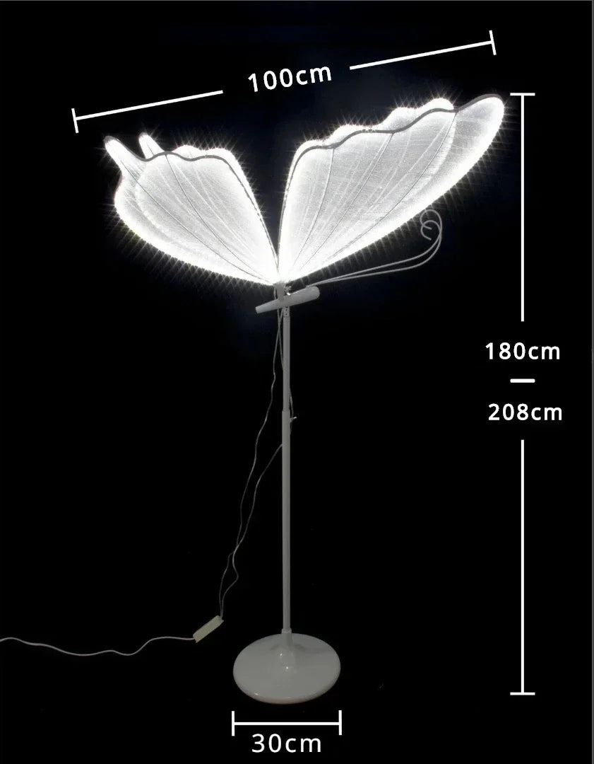 Floor lamp with illuminated butterfly wings. Dimensions: 100cm wide wings, 180cm tall to the top of the wings, 208cm total height, 30cm round base. Set against a black background.