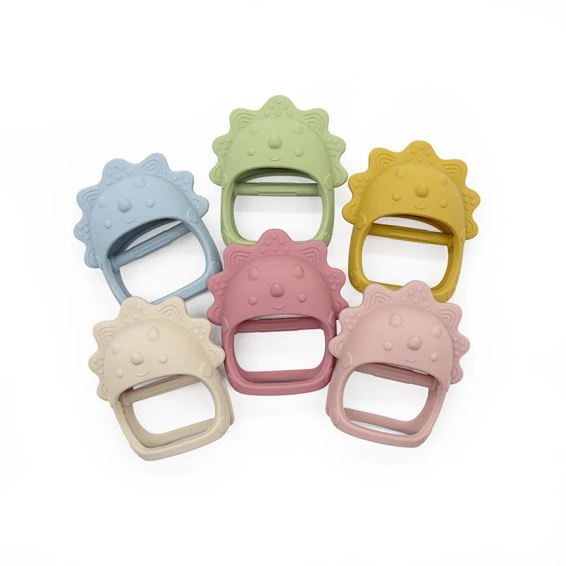 Six colorful dinosaur-shaped baby silicone teethers arranged in a circle. Colors include blue, green, yellow, beige, pink, and mauve. Each teether has a textured surface.