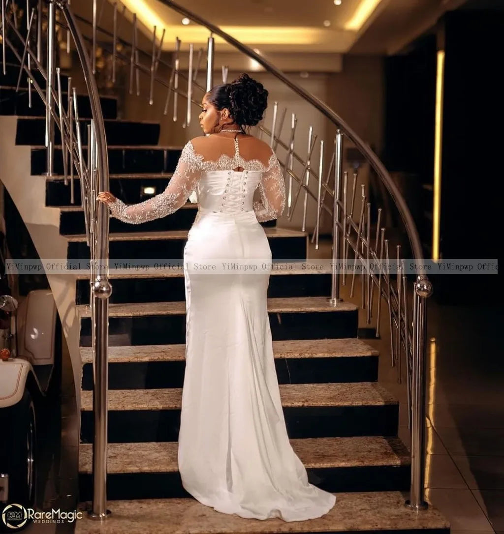 A woman in a long, elegant white gown with lace sleeves stands on a staircase, viewed from the back. The setting is luxurious, with polished railings and warm lighting.