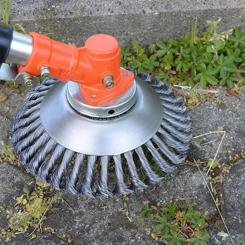 Close-up of a wire brush trimmer head with an orange attachment, cleaning weeds and grass from a concrete surface.