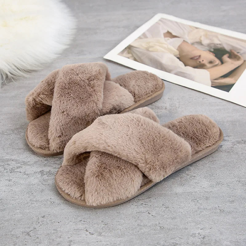 Plush brown slippers with a fluffy crisscross design placed on a gray surface, next to a magazine featuring a person in a white outfit. A white fur rug is partially visible.