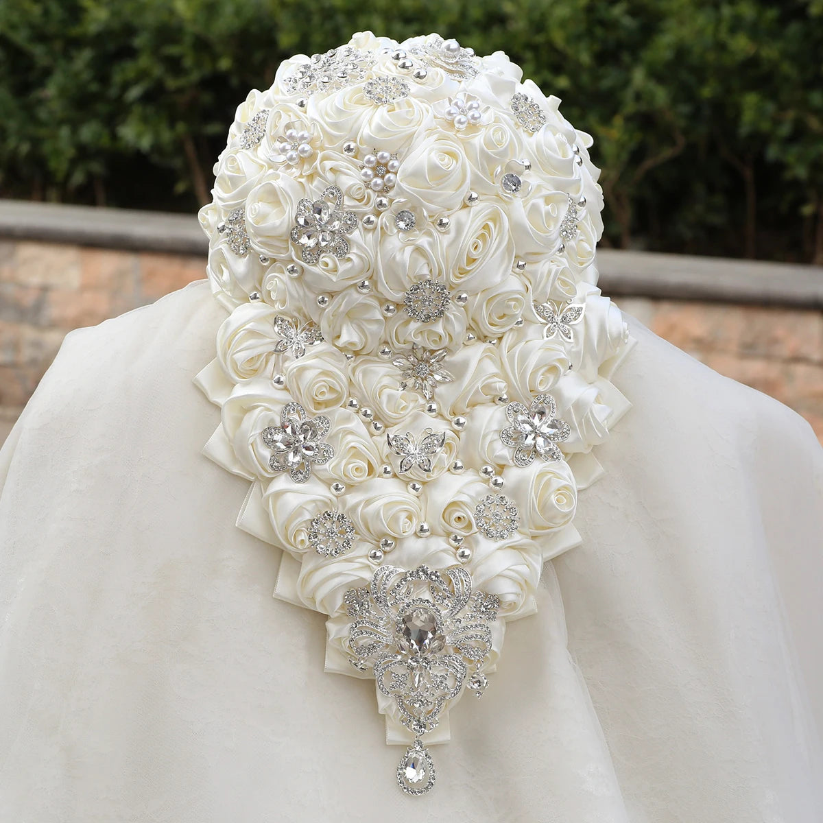 Elaborate bridal headpiece with ivory satin roses and sparkling silver embellishments, including pearls and floral designs, set against a blurred outdoor background.