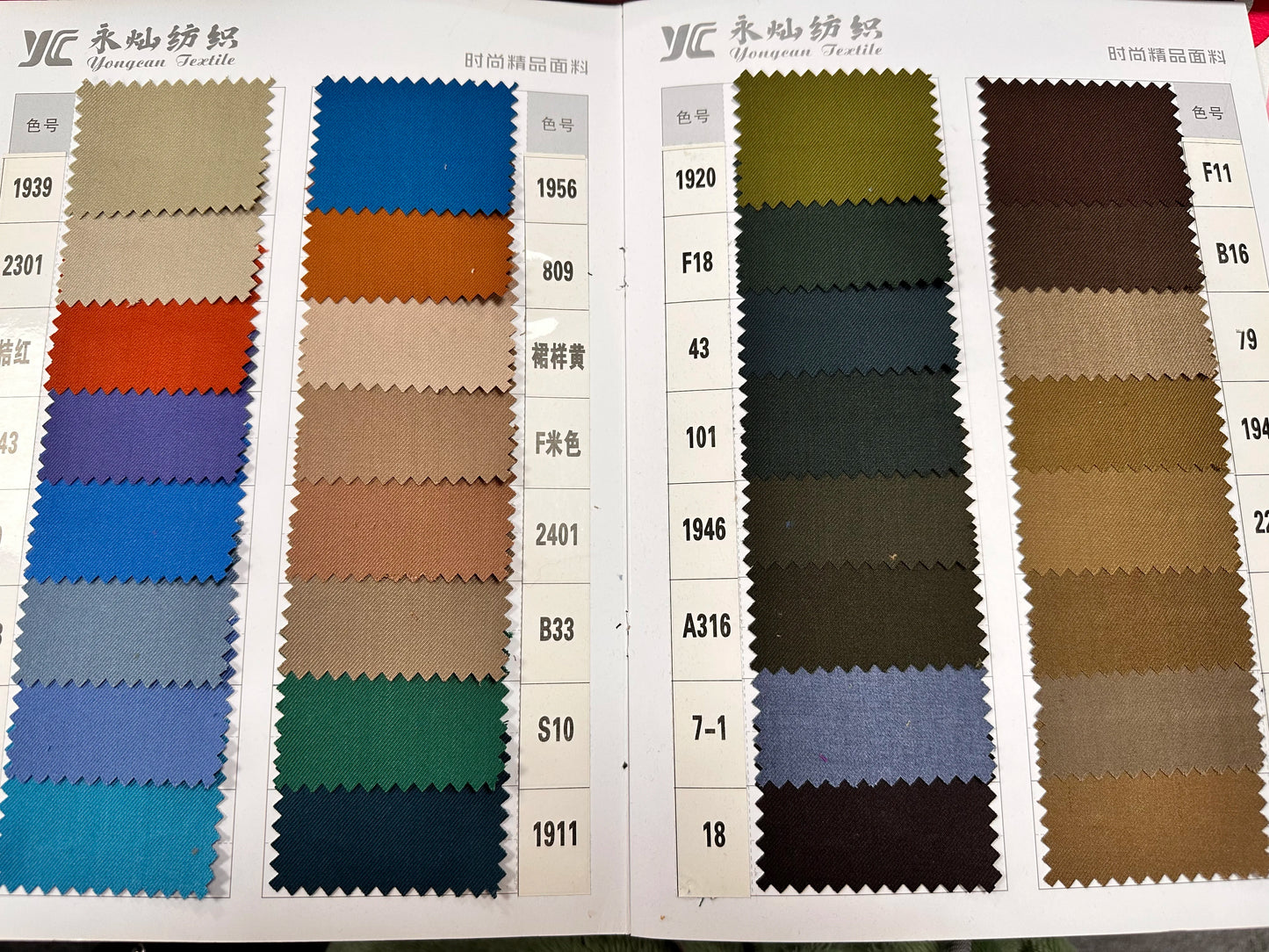 Two fabric sample sheets from Yongean Textile display a variety of colors, including beige, blue, orange, green, brown, and more, each labeled with a color code on the side.