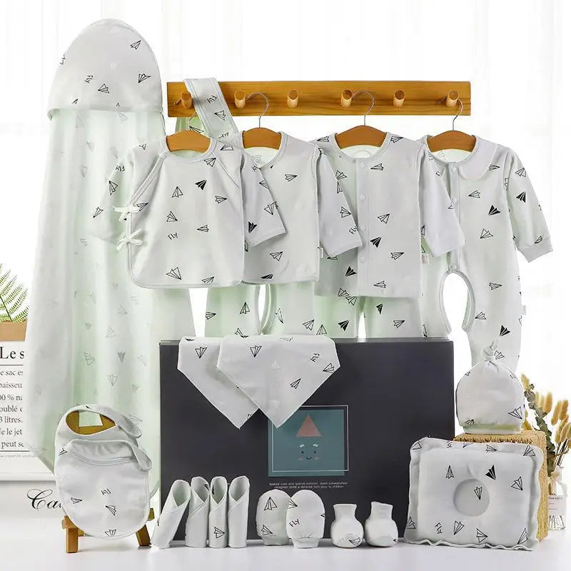 Set of baby clothes and accessories featuring a paper airplane print. Includes onesies, blankets, hats, mittens, booties, and bibs, displayed on hangers and a gift box.