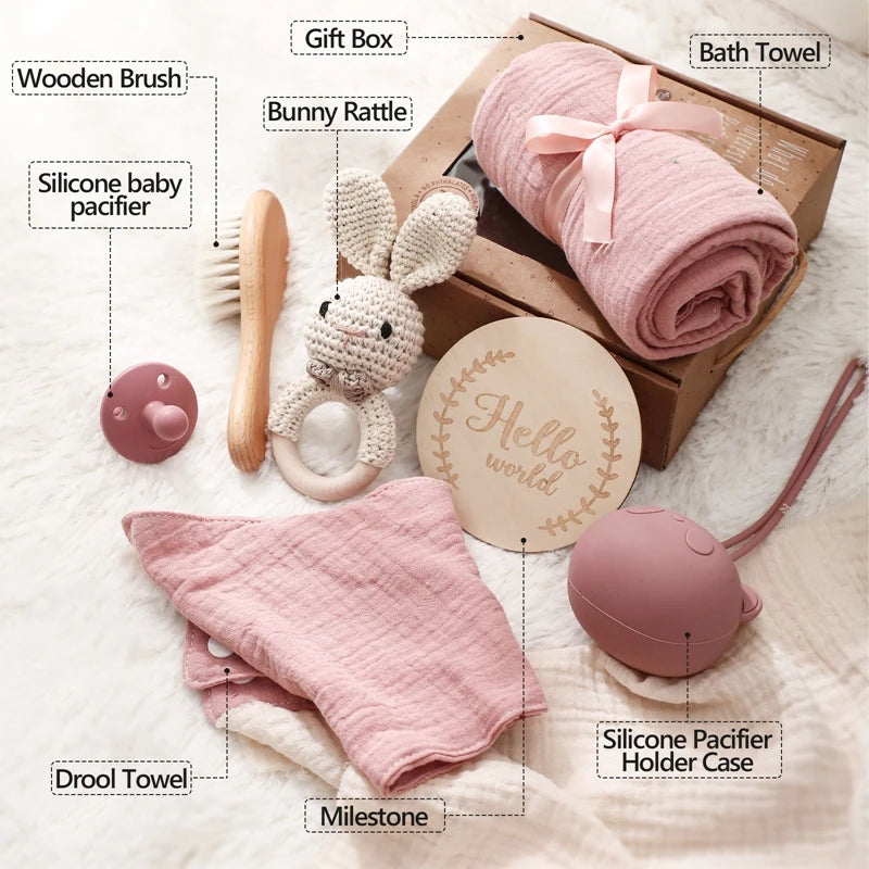 Baby gift set includes a pink bath towel, bunny rattle, wooden brush, silicone pacifier, holder case, drool towel, and "Hello World" milestone disc in a gift box.