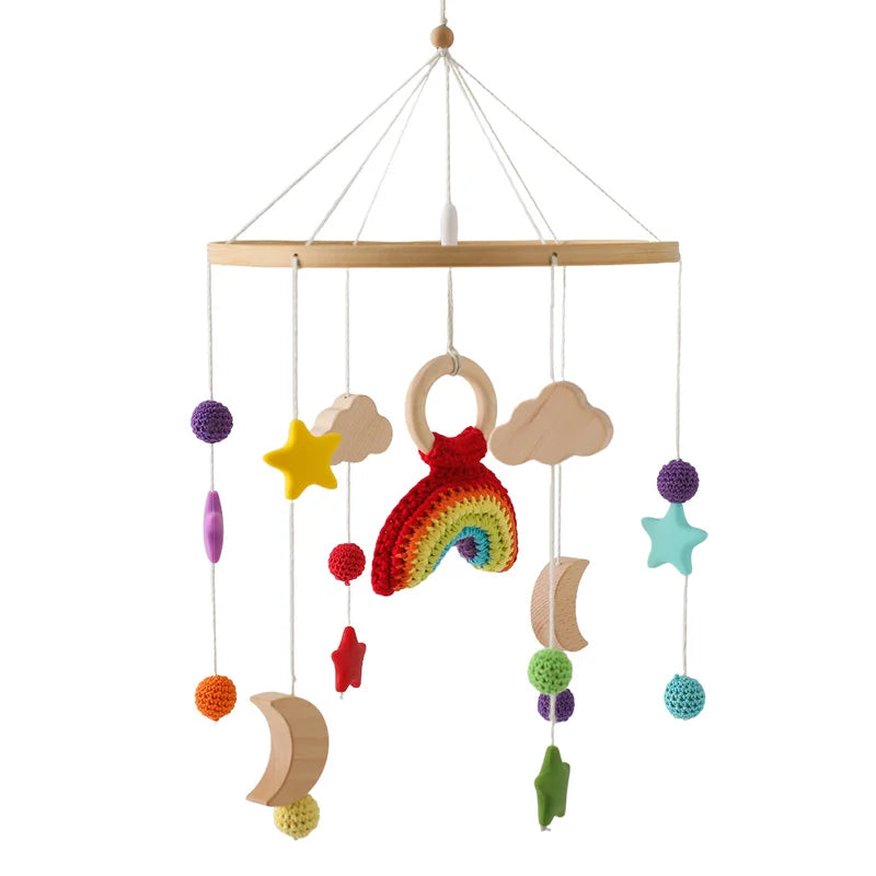 A baby mobile featuring colorful, crocheted stars, moons, clouds, and a central rainbow suspended from a wooden holder. The vibrant elements hang from strings.